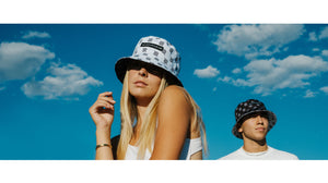 reversible bucket hat on two models black and white hats allreversible brand beach and blue sky in the background